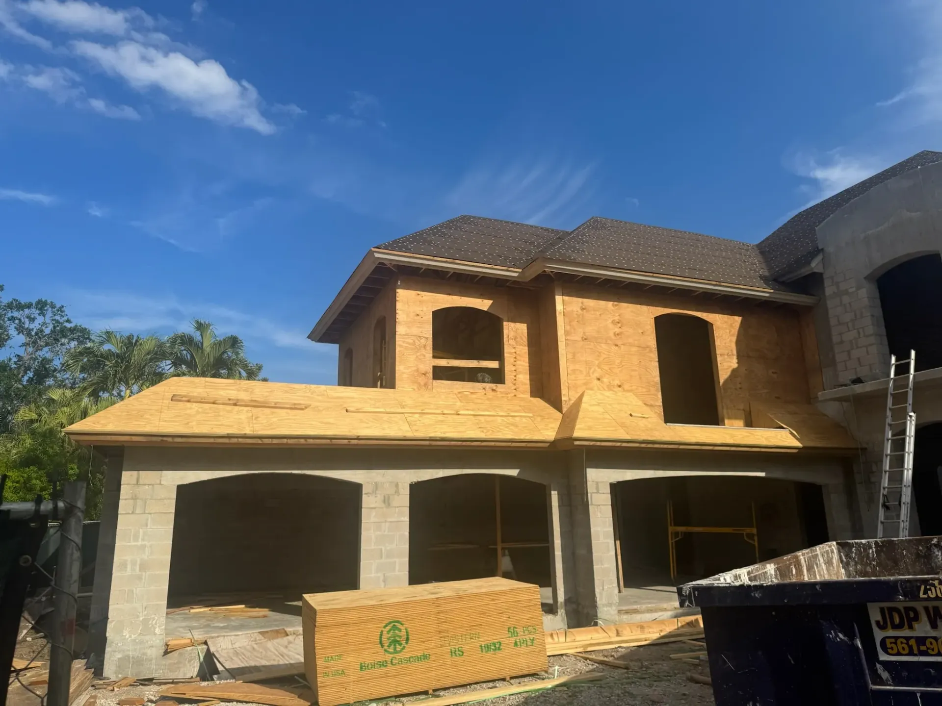 A large house under construction with a dumpster in front of it.