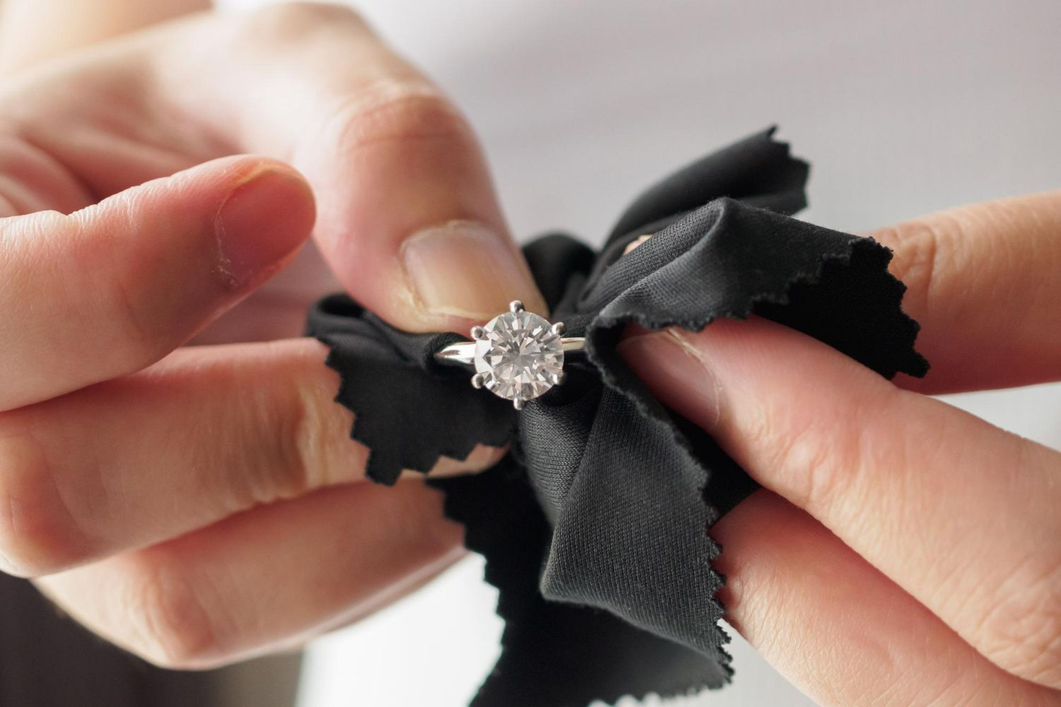 Hands use a soft black cloth to carefully polish a sparkling diamond ring.