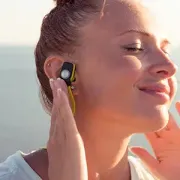 Woman wearing a wireless earbud, eyes closed, enjoying music in bright sunlight