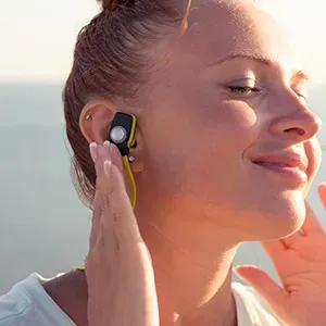 Woman wearing a wireless earbud, eyes closed, enjoying music in bright sunlight