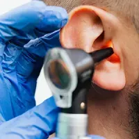 Doctor examining ear with an otoscope while wearing blue gloves