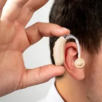 Close-up of a person fitting a behind-the-ear hearing aid onto an ear.