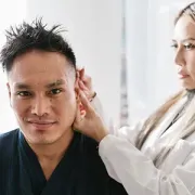 Woman touching a man’s ear during a grooming or medical check in a bright room