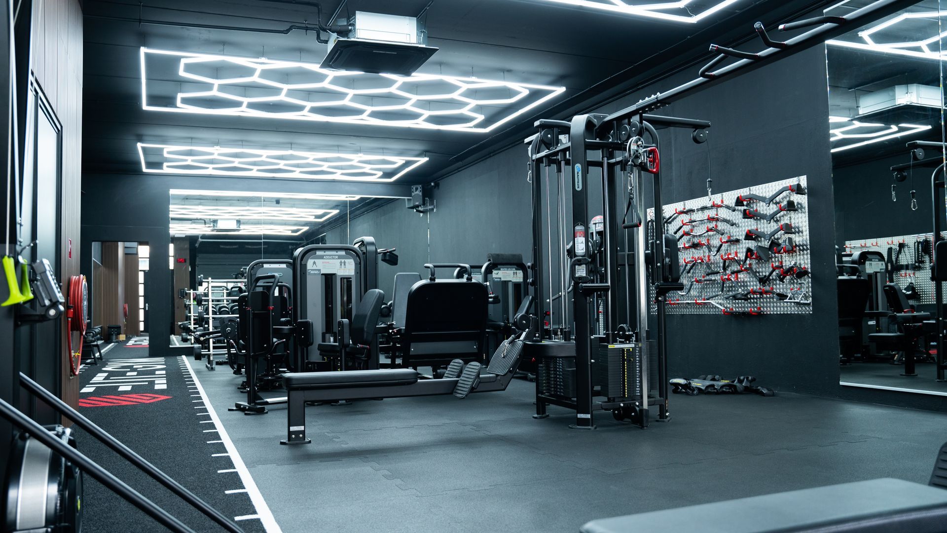 Interieur van een sportschool met donkere muren, fitnessapparatuur en zeshoekige plafondlampen.