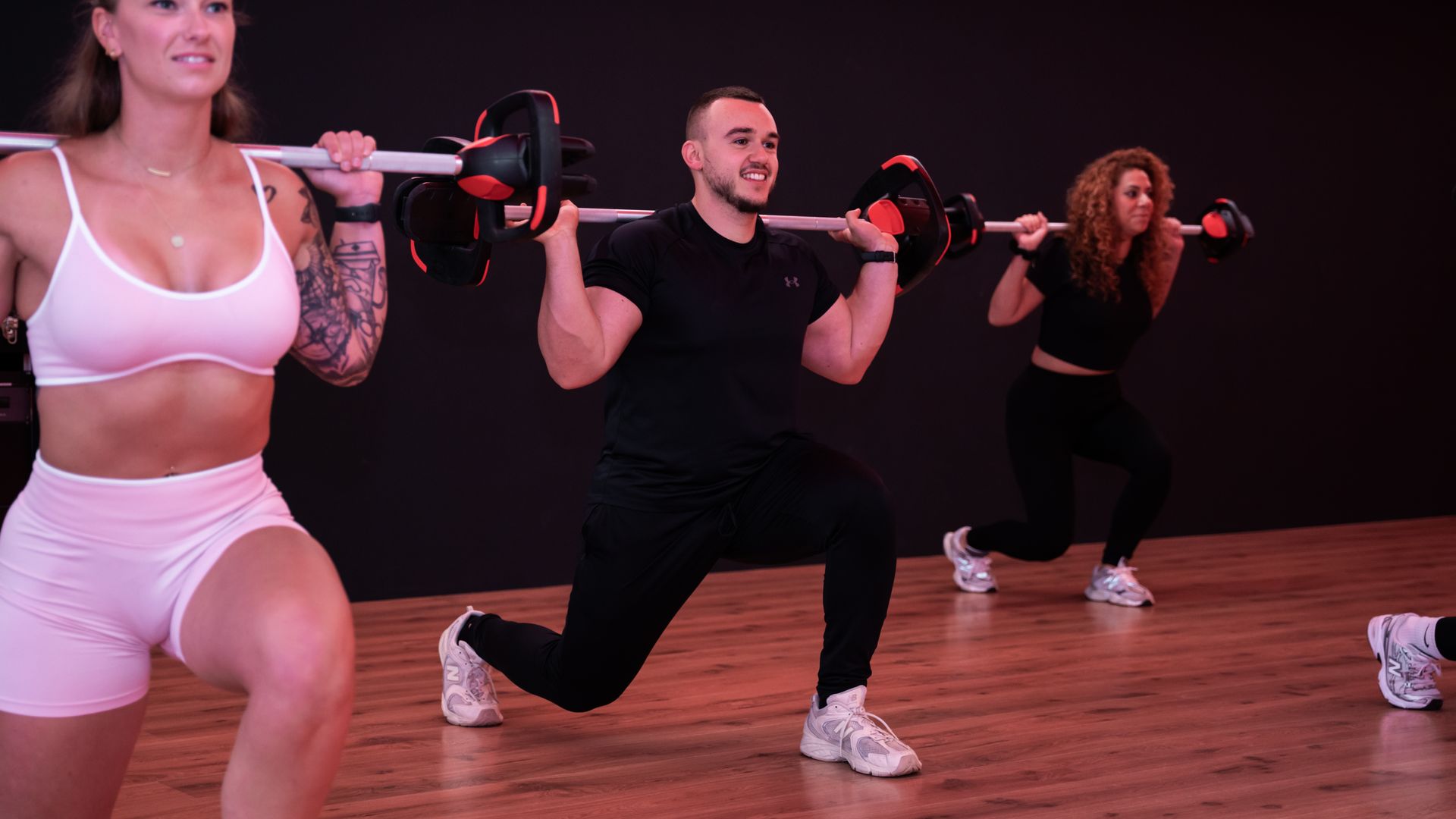 Mensen in een sportschool die lunges doen met verzwaarde stangen. Donkere omgeving.