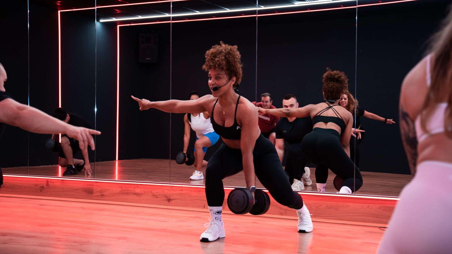 Een vrouw traint met dumbbells in een sportschool. Ze staat in een uitvalspositie met gestrekte arm.