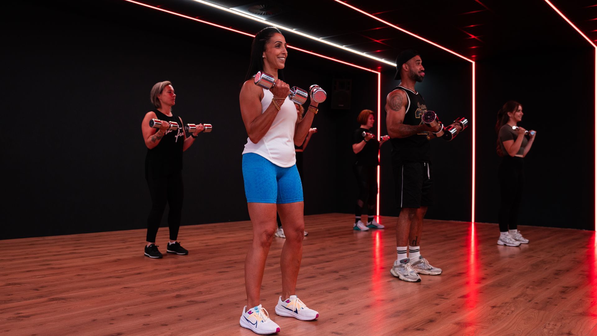 Groepsoefeningen met dumbbells in een studio. Rode en witte lampen verlichten de ruimte.