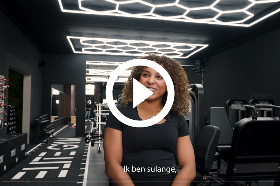 Een vrouw in een zwart shirt in een sportschool, pratend. Modern, zwart interieur met fitnessapparatuur.