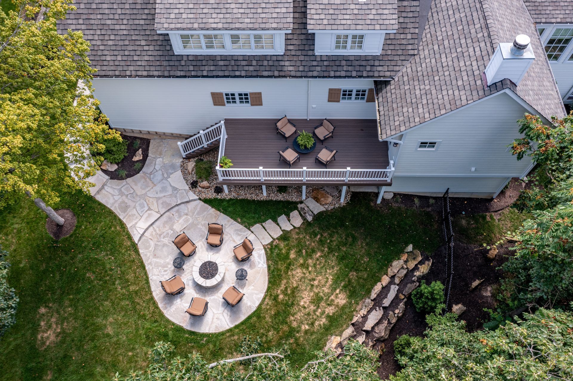 Aerial view of a backyard patio with round table, chairs, deck seating, and stone fire pit area