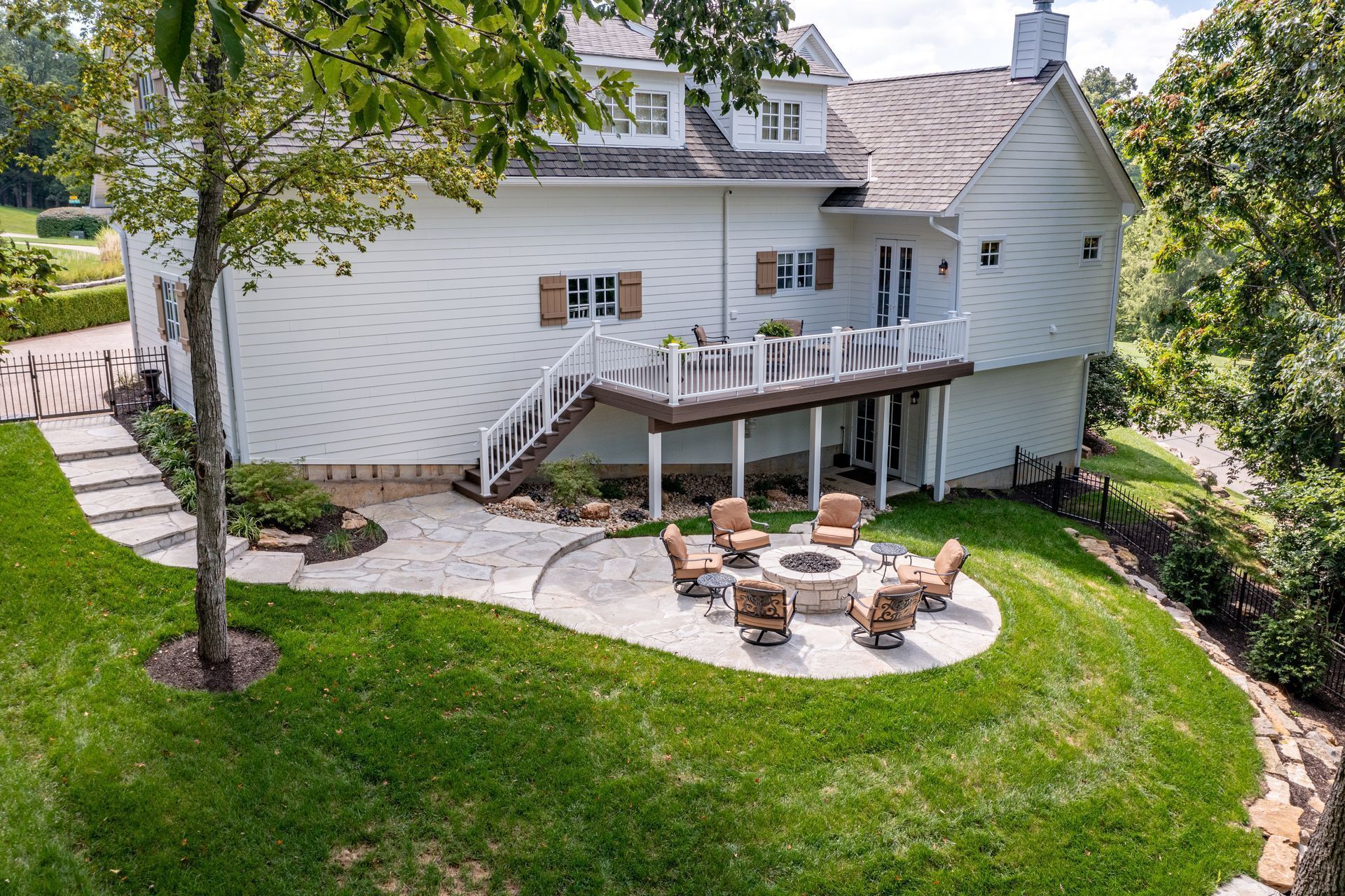 White house with a raised deck and stone patio seating in a green backyard