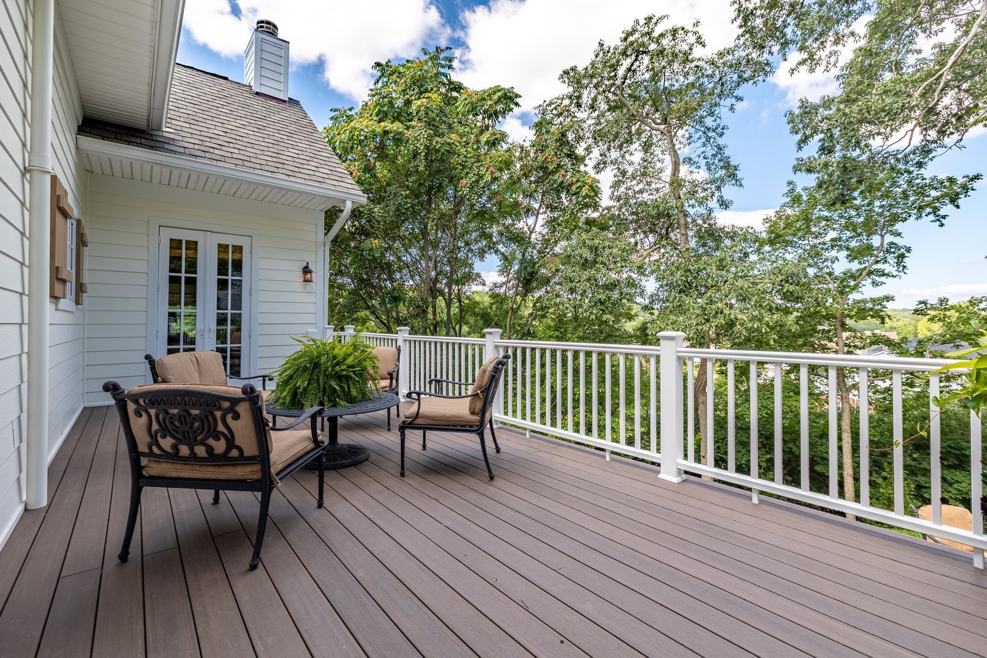 Wooden deck with patio chairs and white railing overlooking trees and a cloudy sky