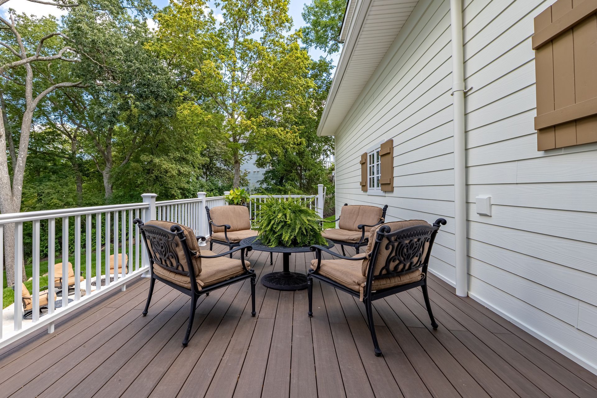 Outdoor deck with wicker chairs, round table, and white railing beside a house and trees