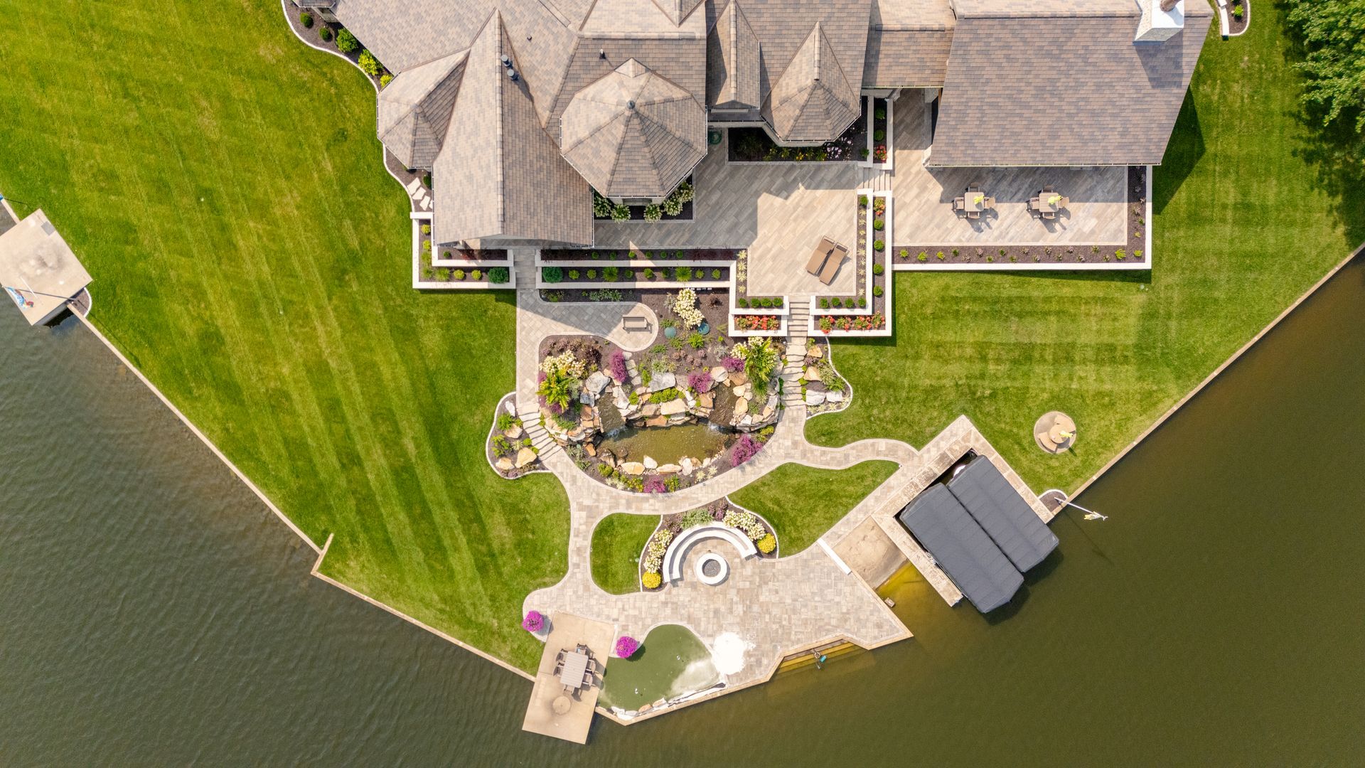 Aerial view of a lakeside house with a landscaped backyard, patio, and dock.