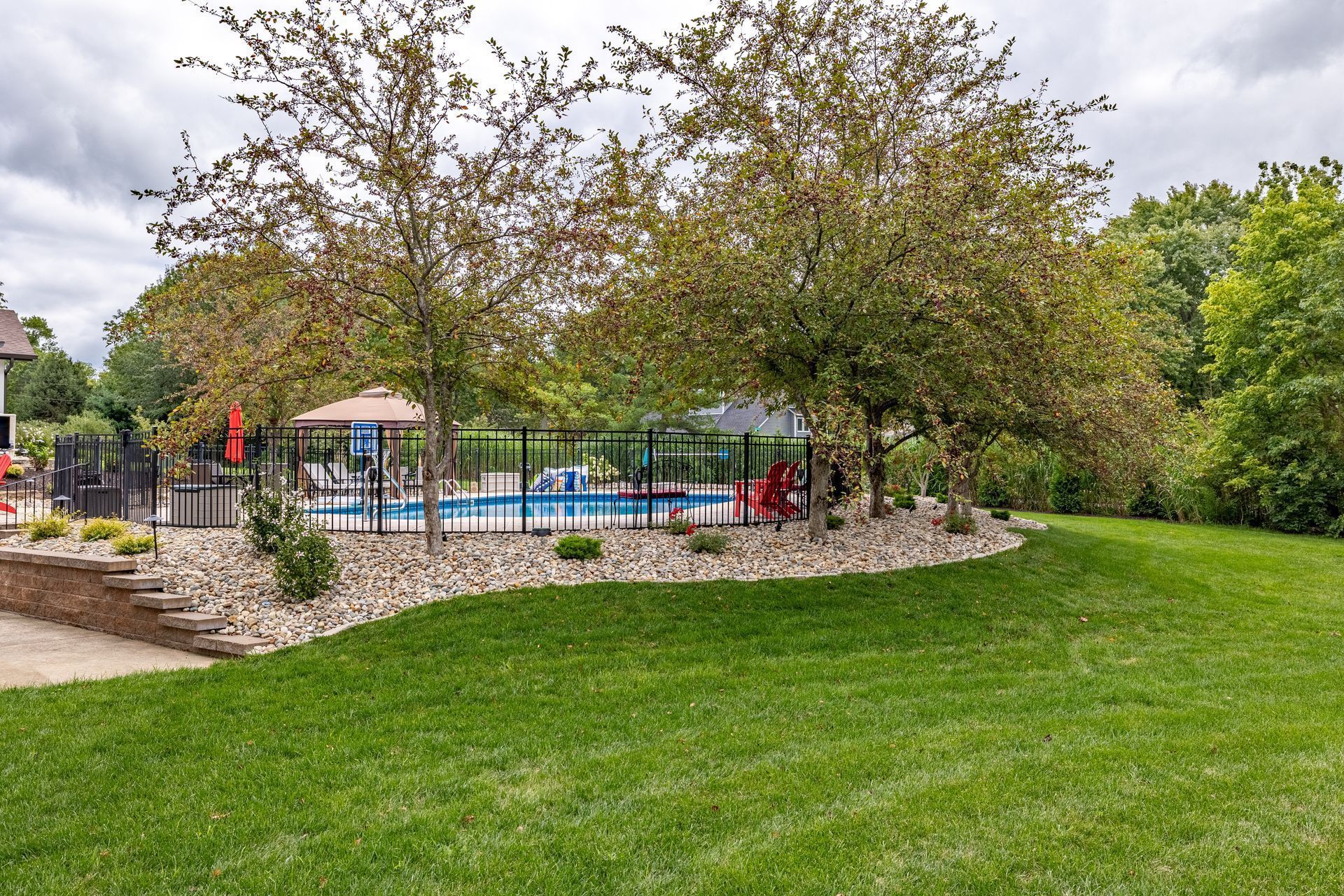 A large lawn with a pool in the background and trees in the foreground.