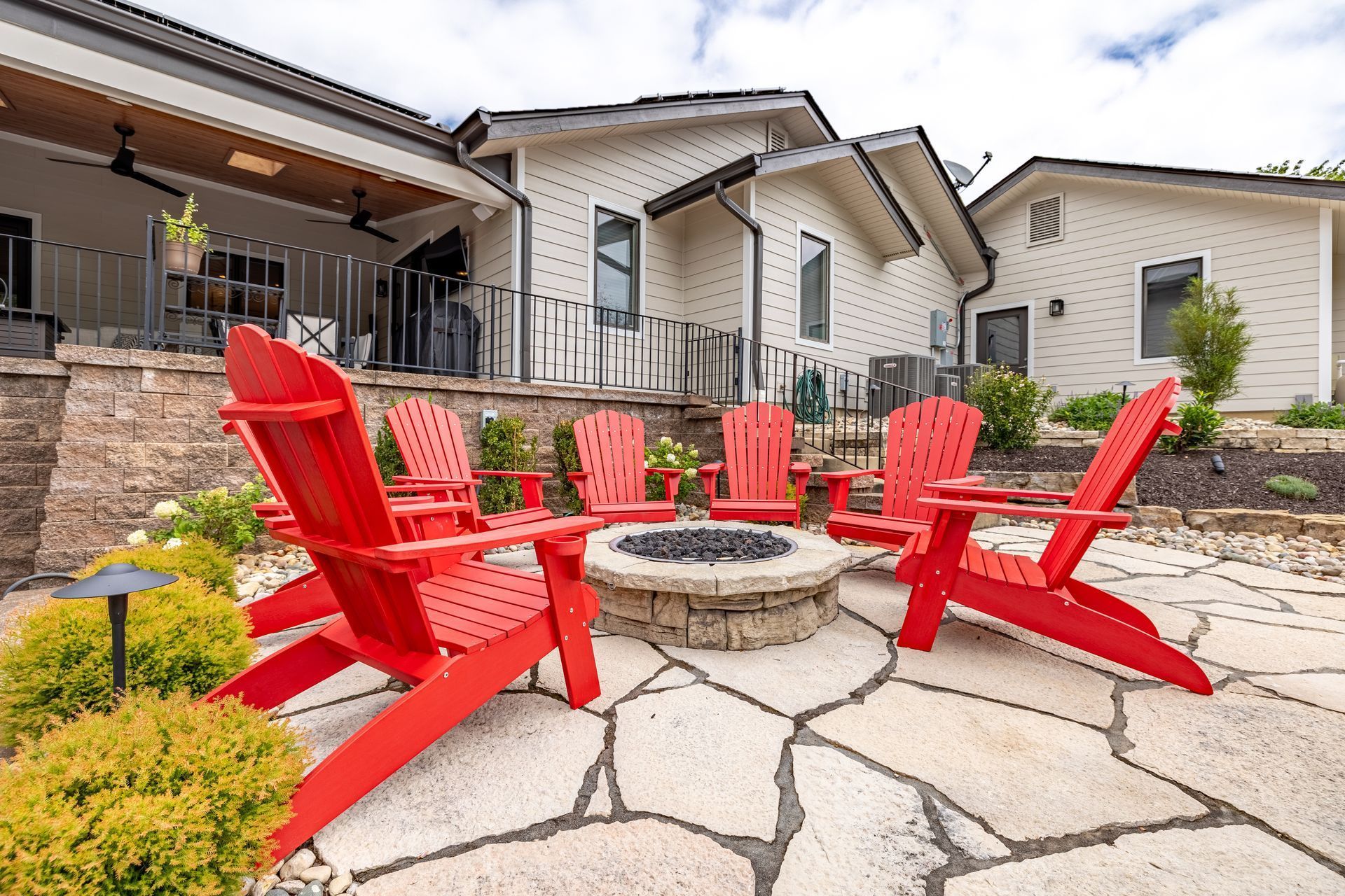 A patio with red chairs and a fire pit in front of a house.