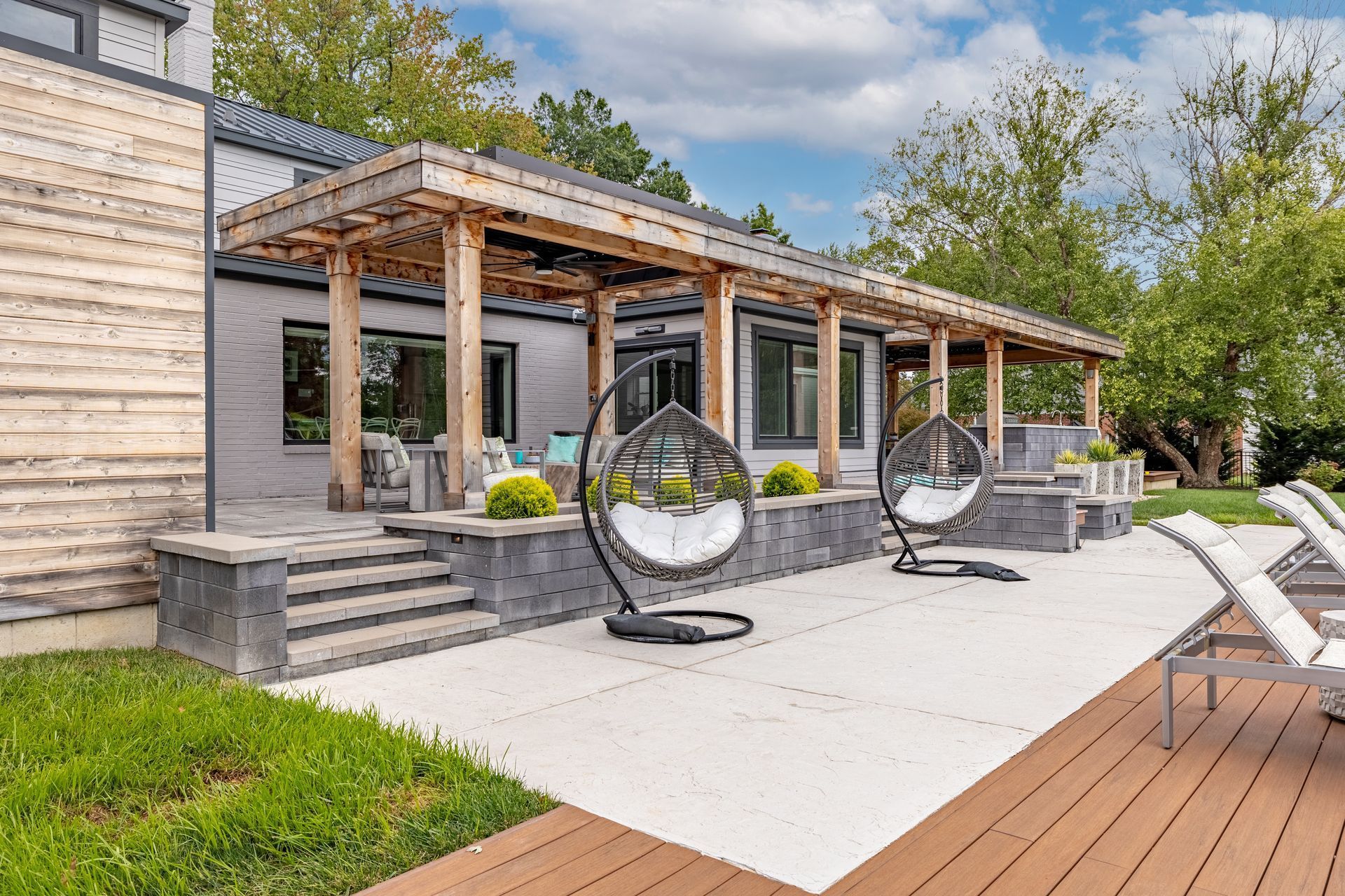 A patio with a pergola and hanging chairs in front of a house.