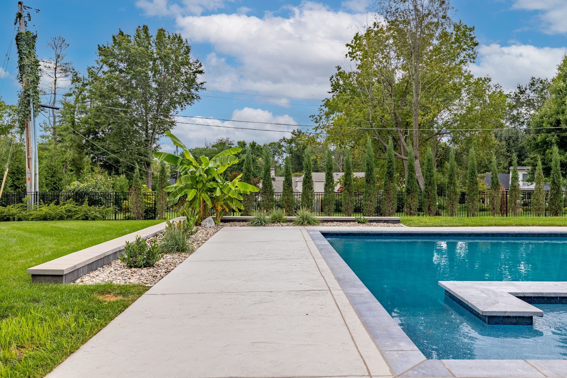 A large swimming pool is surrounded by trees and a concrete walkway.
