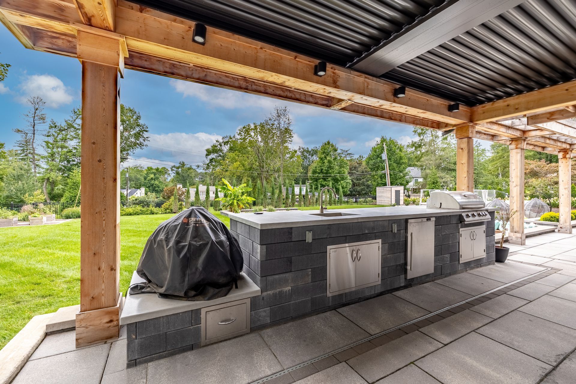 A large outdoor kitchen with a grill and sink under a pergola.