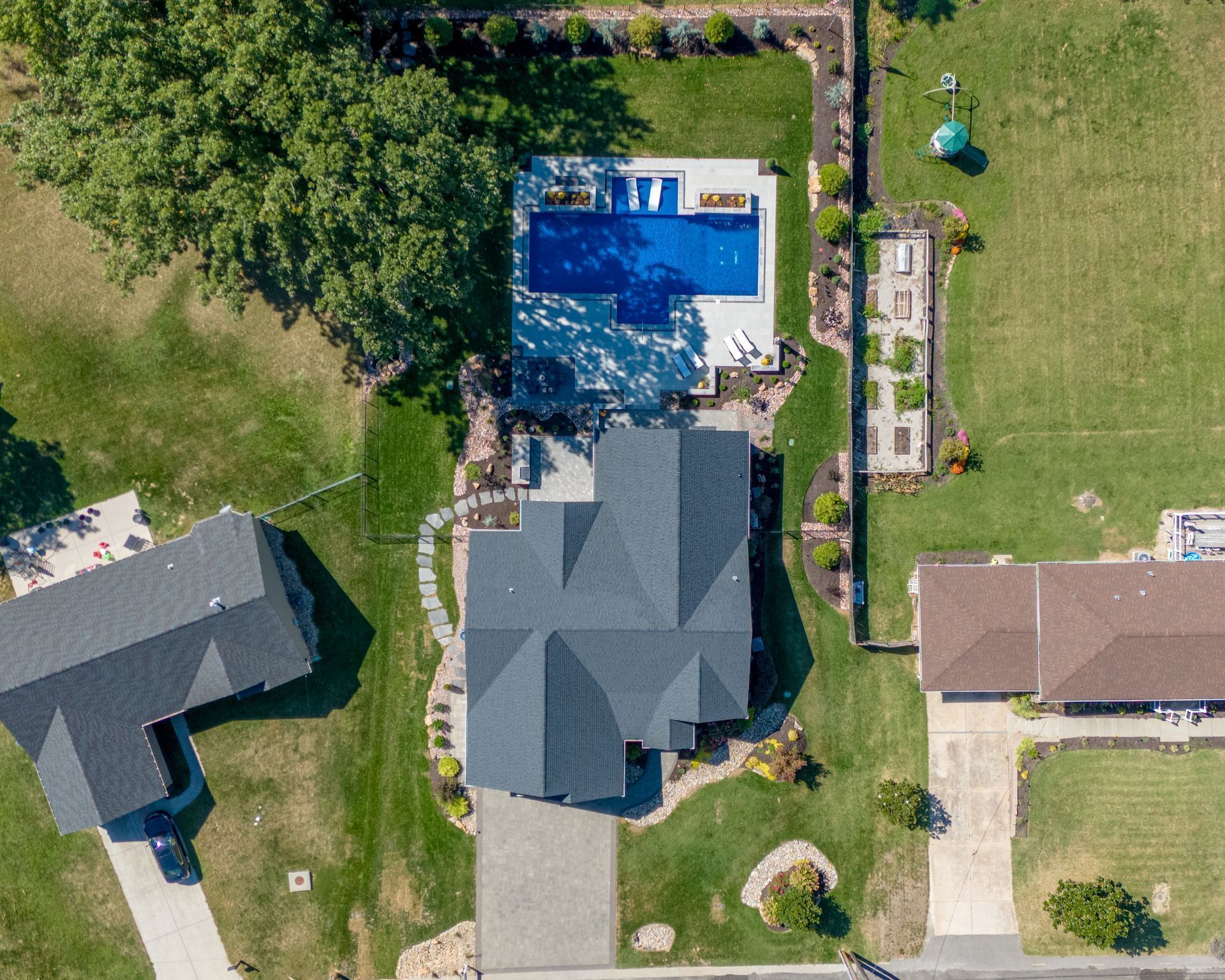 Aerial view of a suburban house with a blue swimming pool, driveway, and neighboring homes.