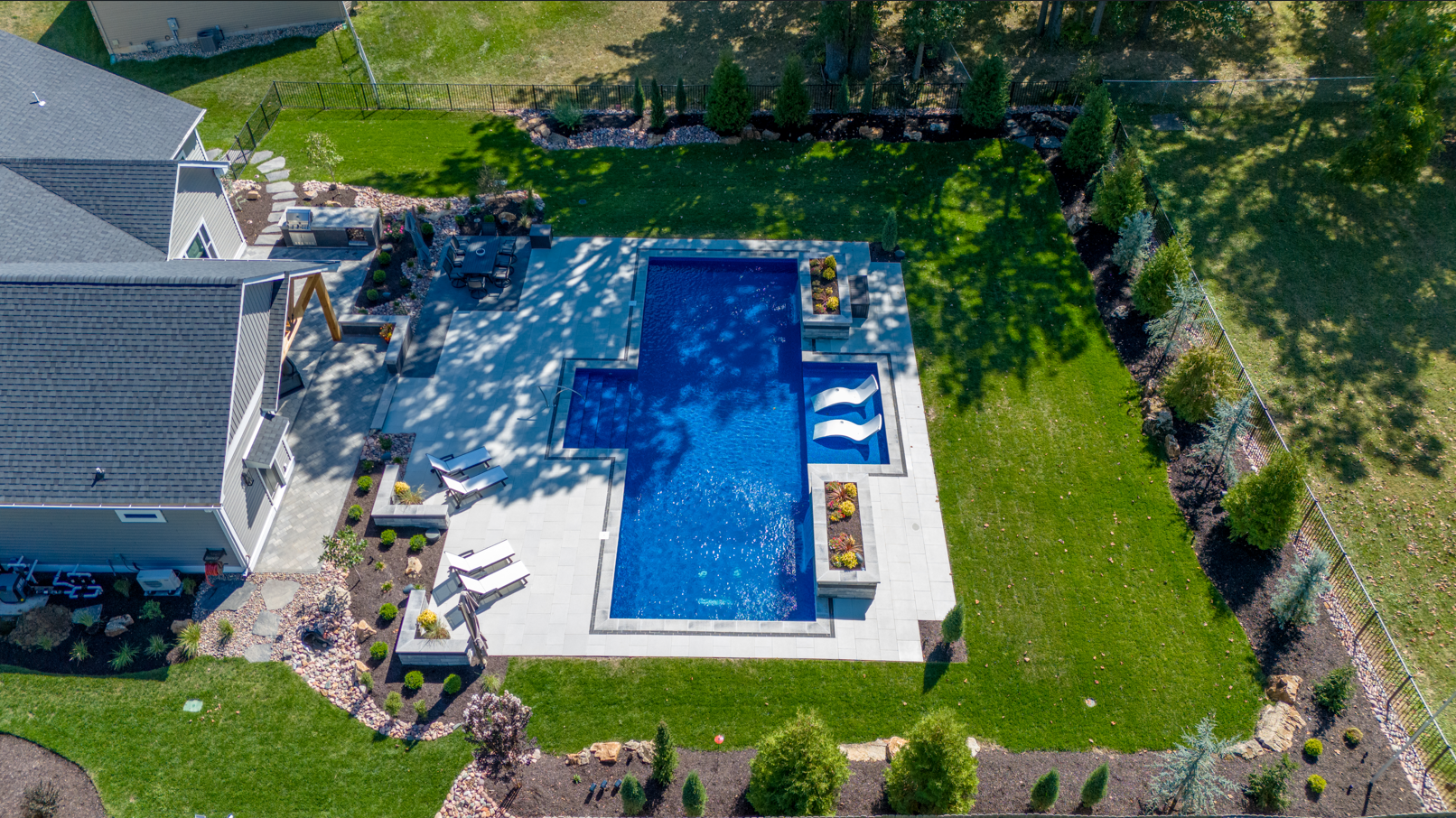 Aerial view of a backyard with a blue rectangular swimming pool, patio, and surrounding greenery