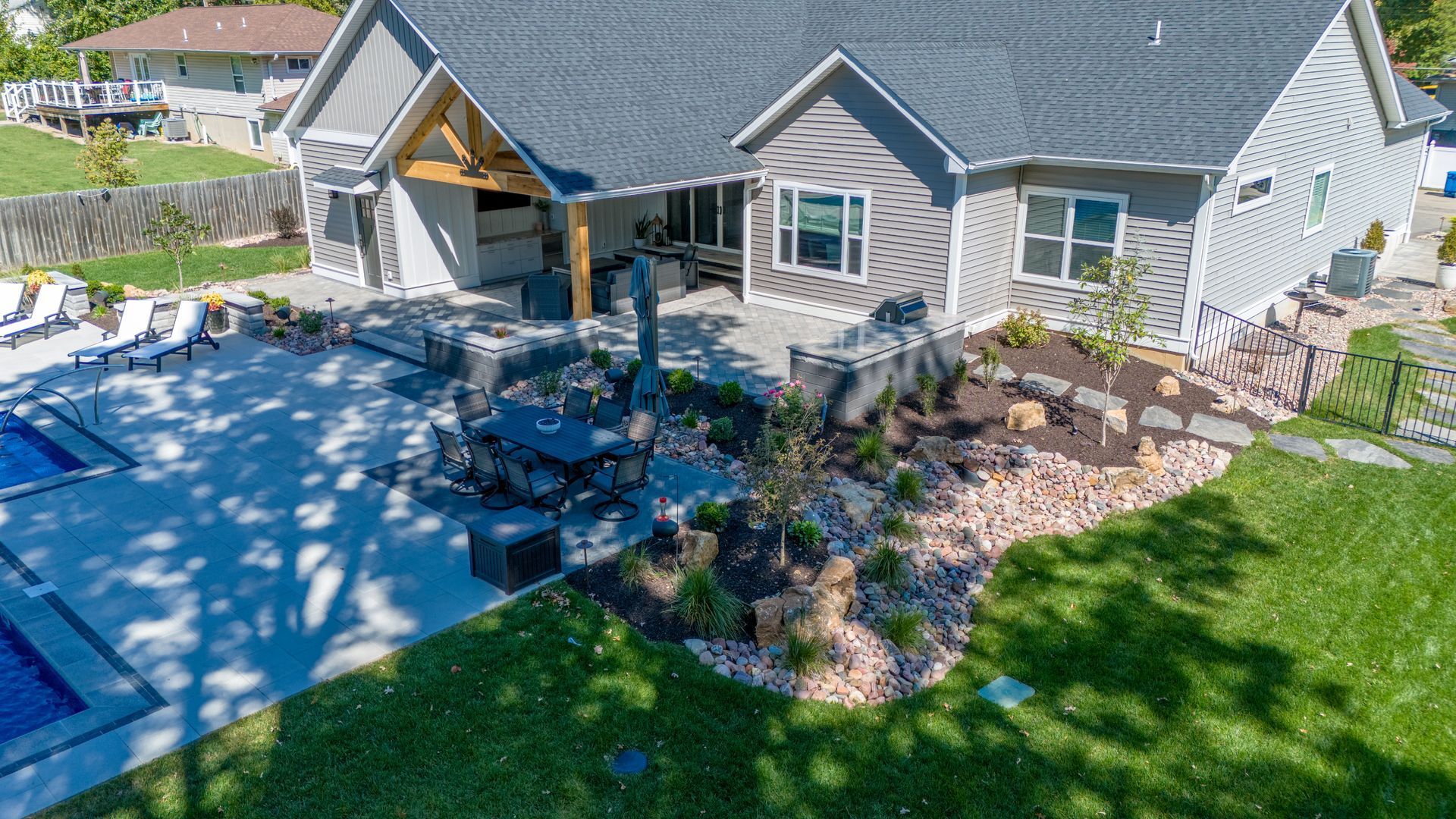 Backyard patio with stone seating area, umbrella, and landscaped garden beside a gray house