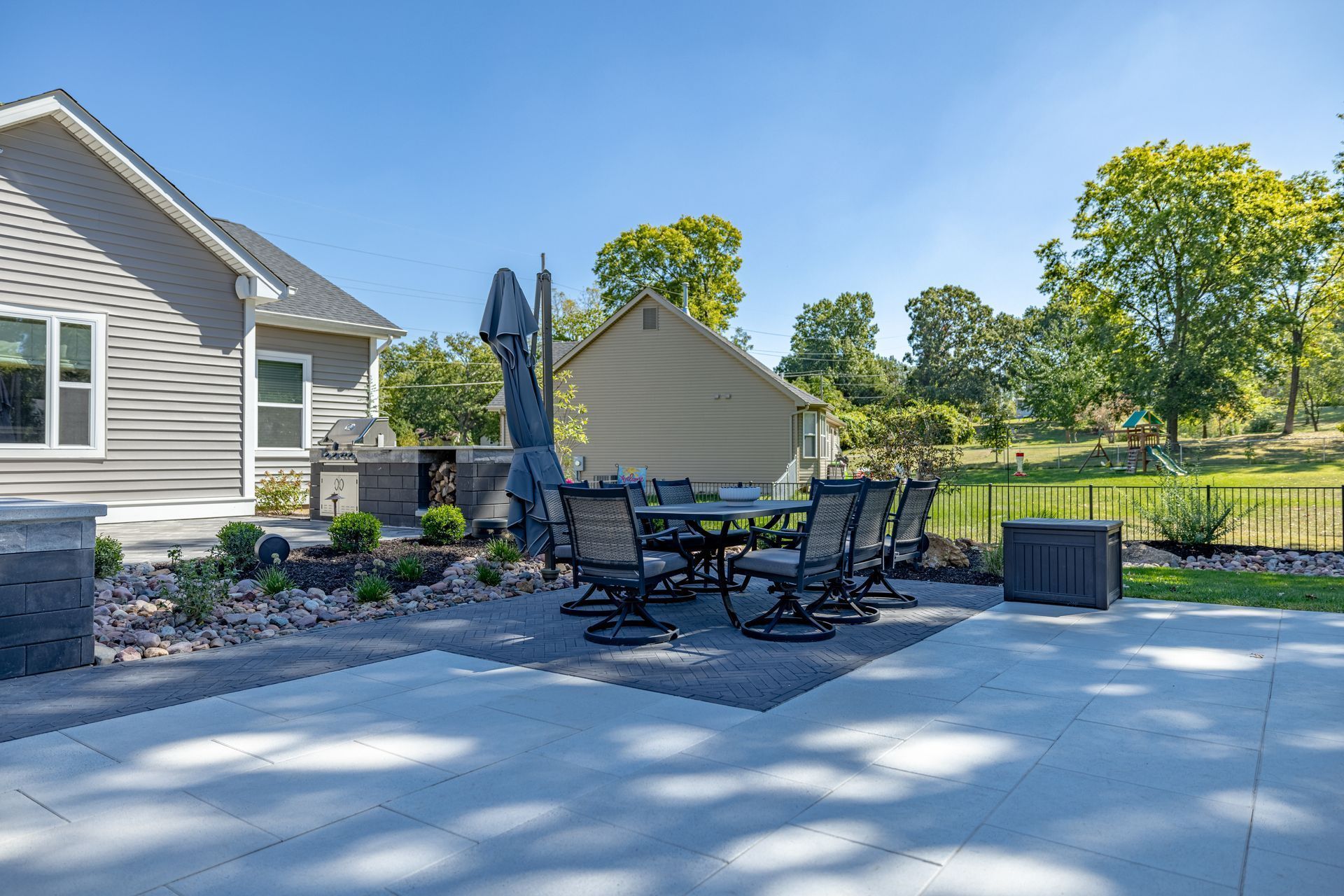 Patio with outdoor dining set, closed umbrella, landscaping, and a backyard lawn beside a house