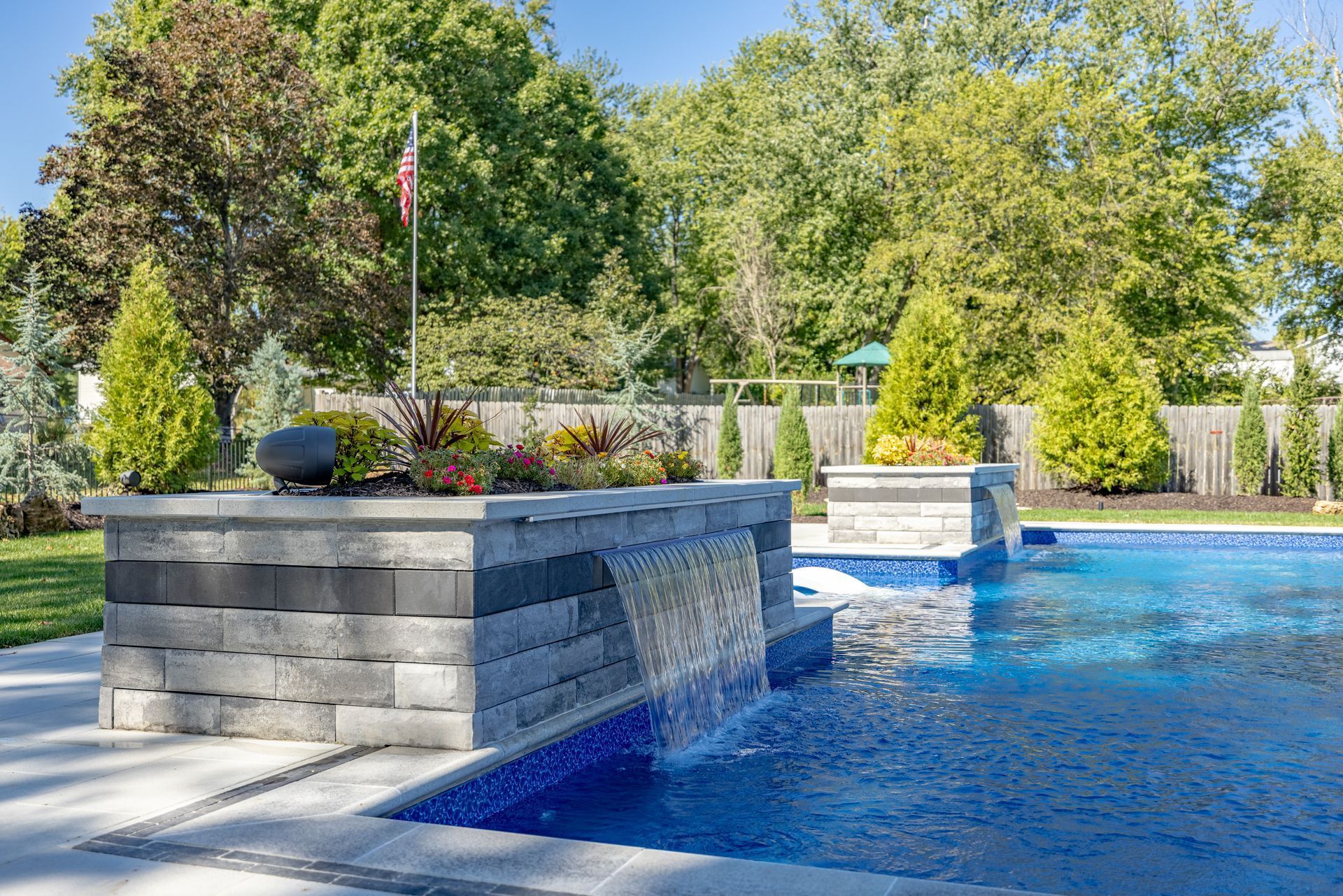 Backyard pool with stone waterfall walls, blue water, and trees in the background