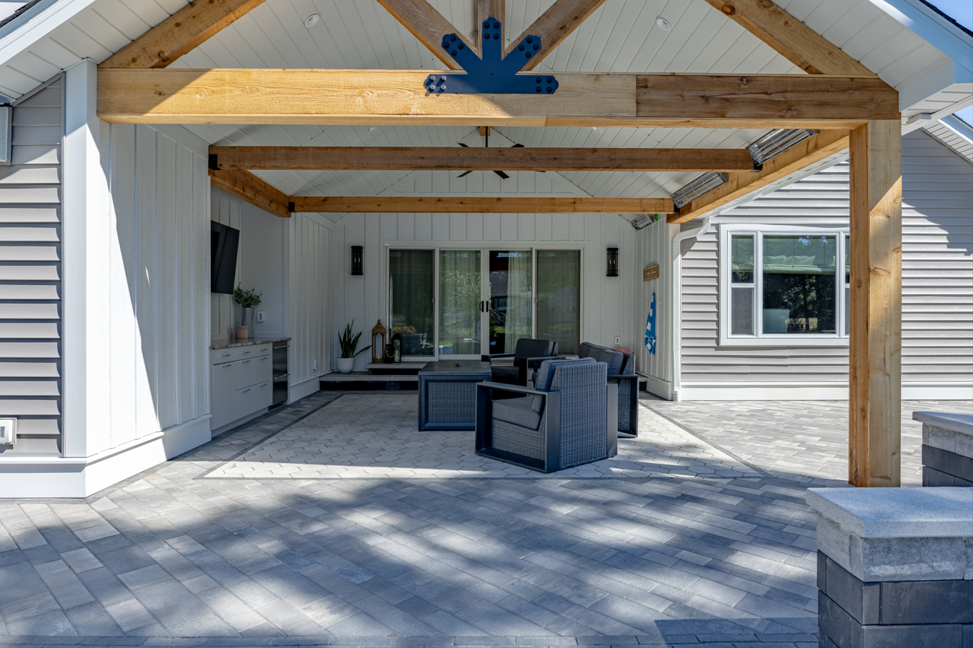 Covered patio with wooden beams, cushioned chairs, and sliding glass doors at a house