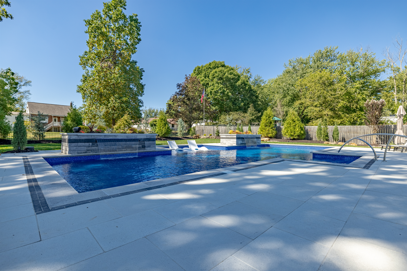 Modern outdoor swimming pool with blue water, tiled deck, and trees under a clear sky