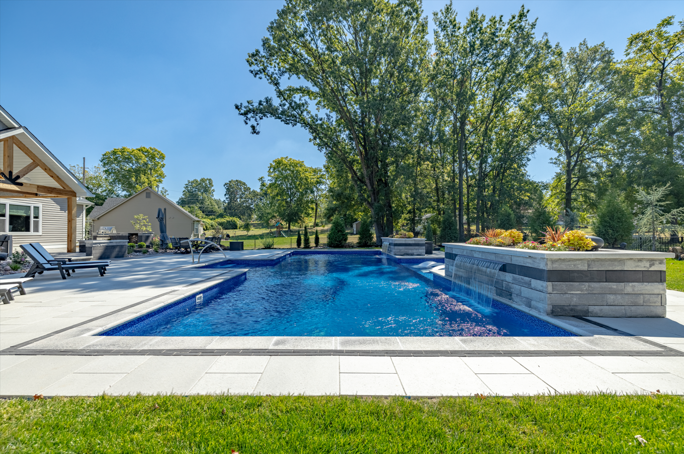 Backyard swimming pool with blue water, stone waterfall, and lounge chairs under trees