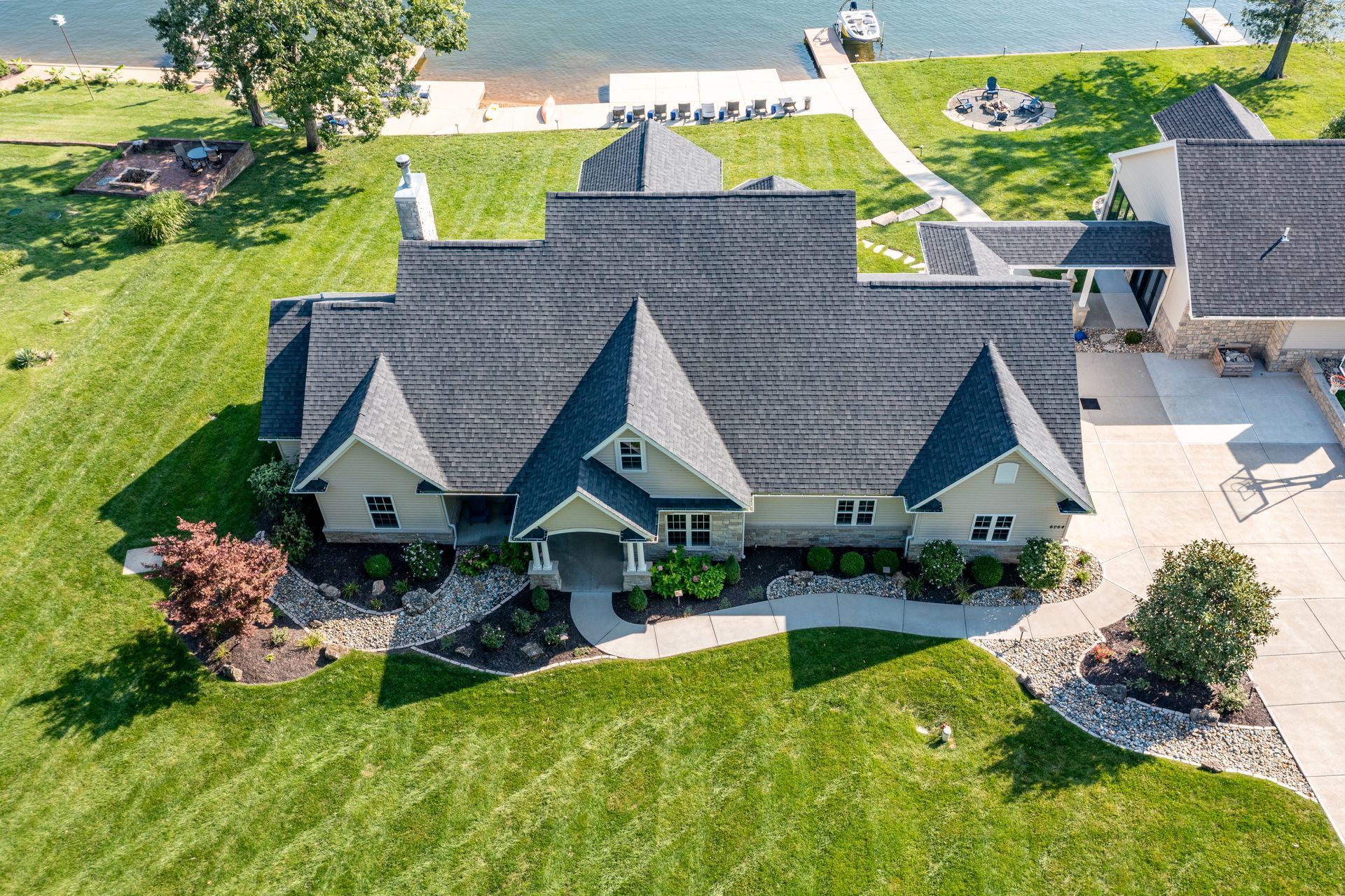 Aerial view of a gray-roofed suburban house with a large green lawn and driveway