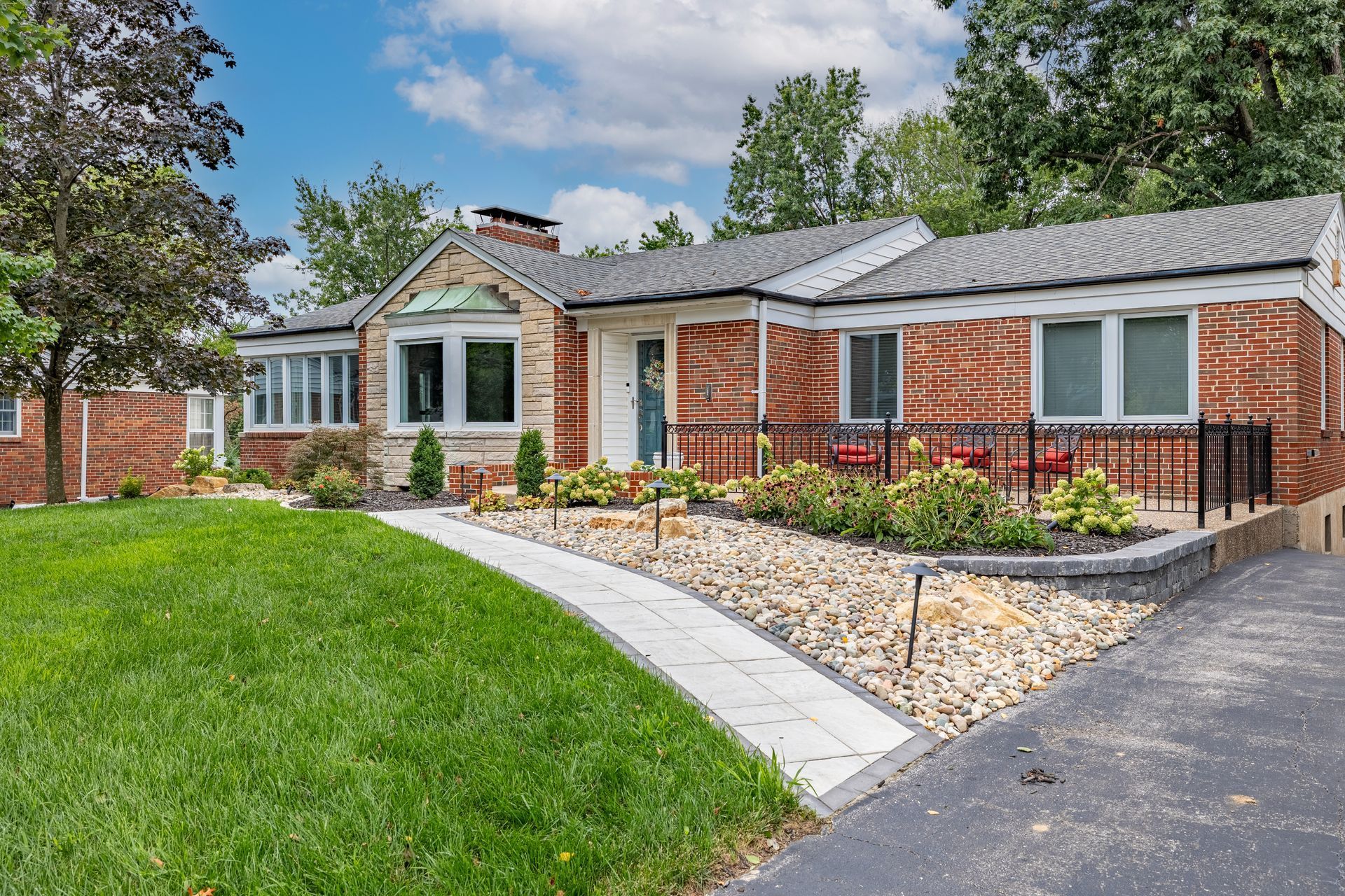 Brick ranch-style house with a manicured lawn, curved walkway, and black railing by the driveway