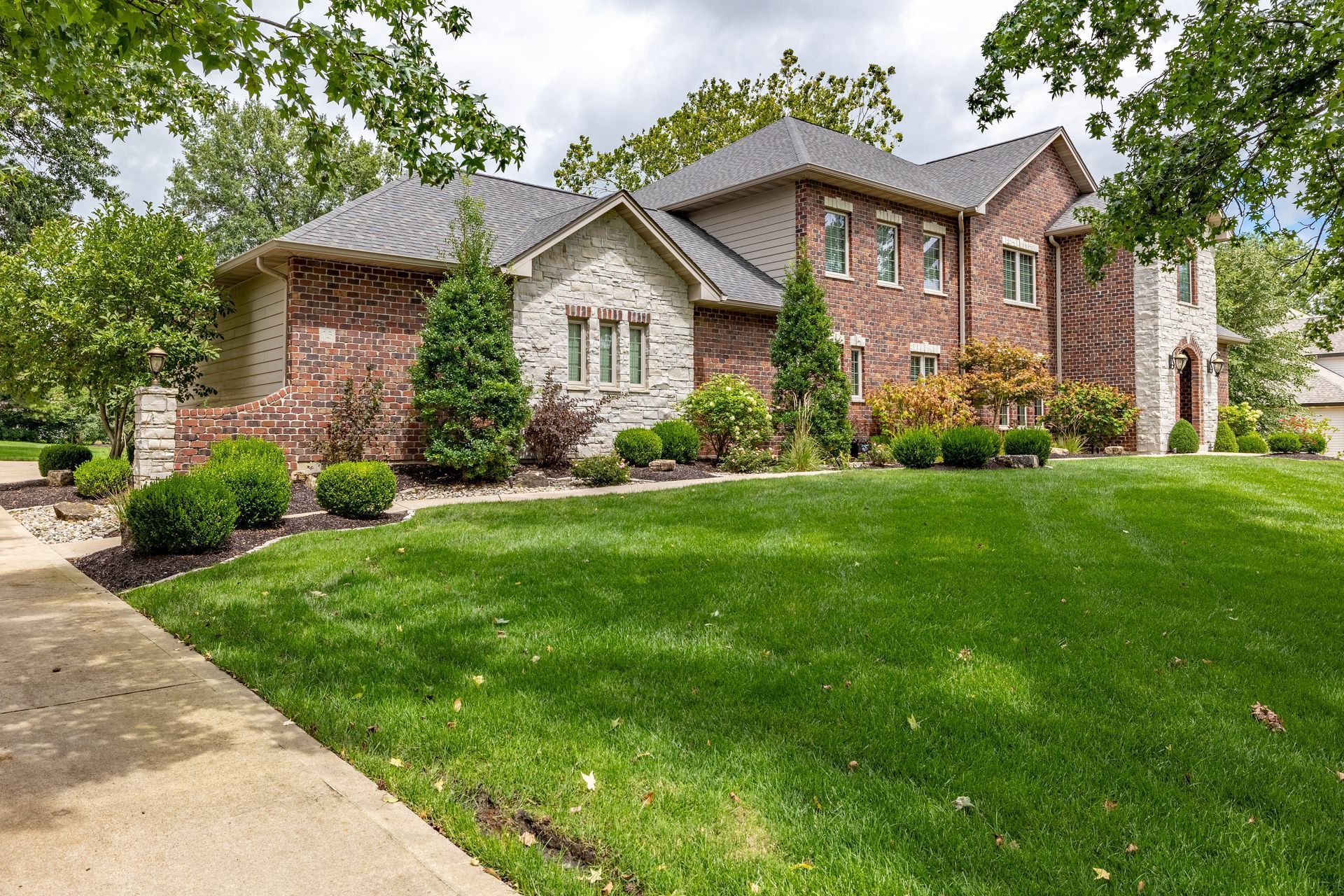 Brick suburban house with manicured lawn and landscaped front yard under cloudy sky