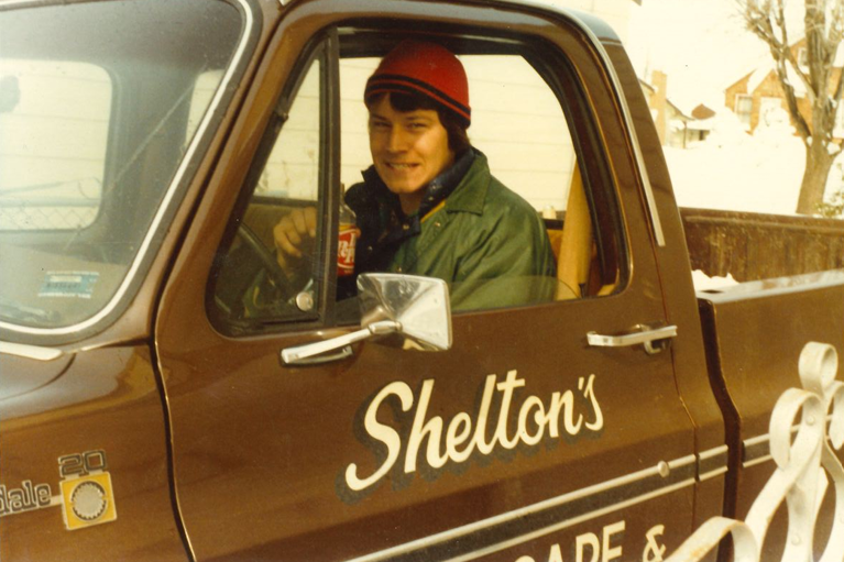 Person in a green jacket and red beanie sits in a brown Shelton’s truck cab.