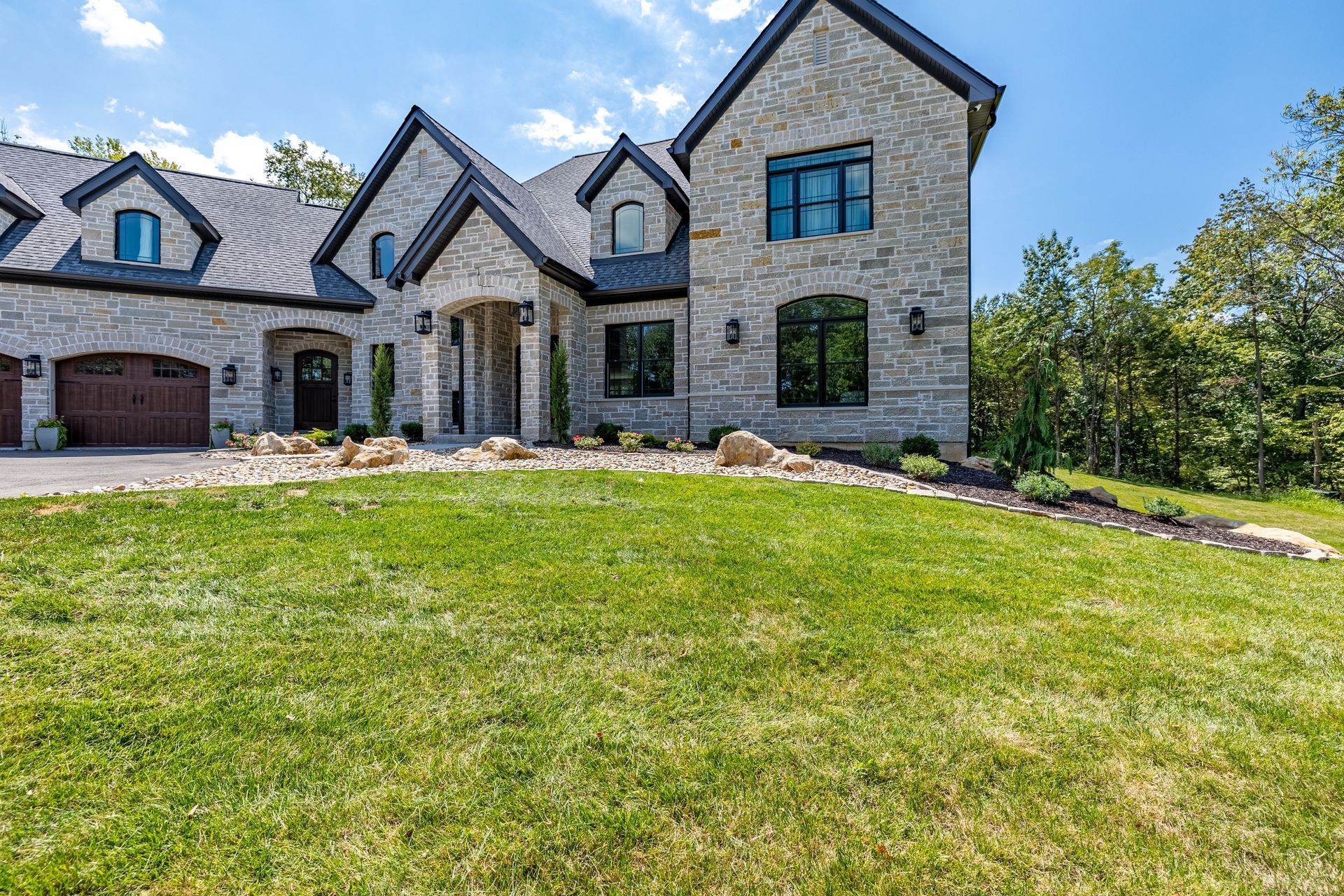 Stone suburban house with blue-trimmed roof and large green lawn under a bright sky