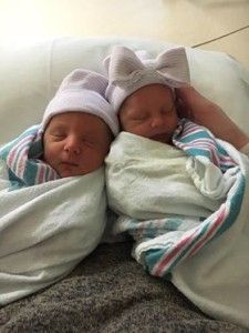 two newborn babies wrapped in blankets and hats are laying next to each other on a couch .