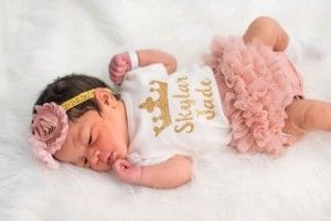 a newborn baby girl wearing a crown and a headband is laying on a bed .