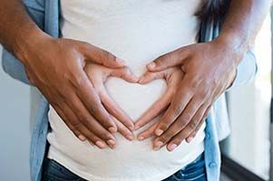 a man and a woman are making a heart shape with their hands on a pregnant woman 's belly .