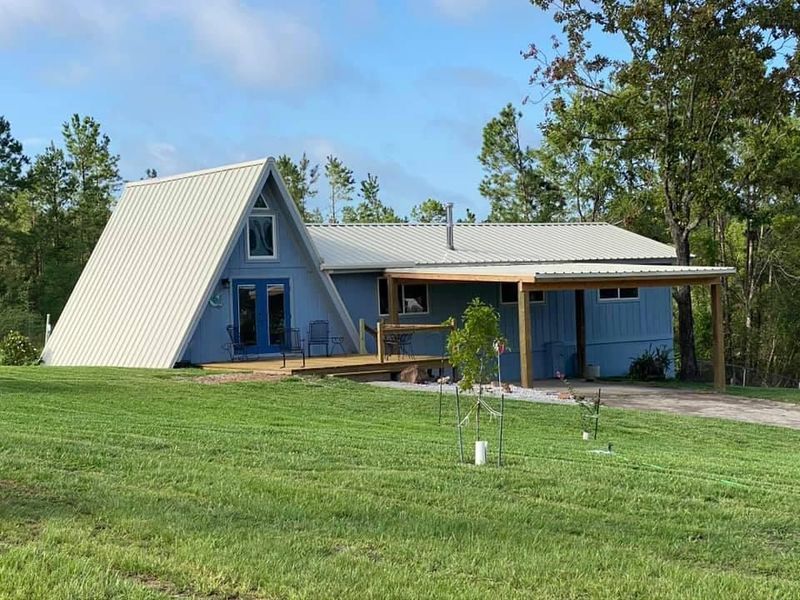 Blue A-frame house with a metal roof on a grassy lawn.