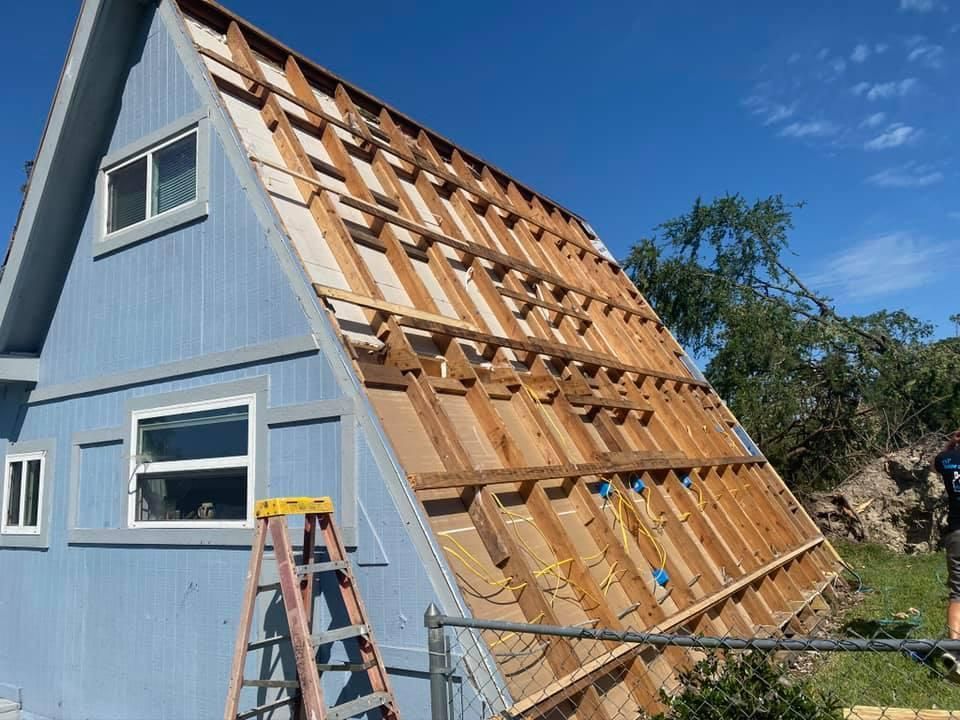 A-frame house with exposed wooden framing and blue siding. A ladder is visible.