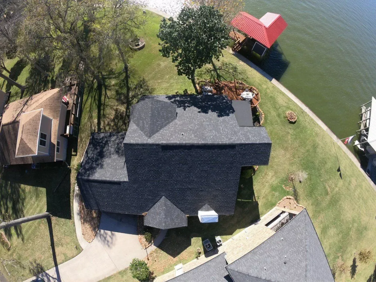 Aerial view of a house with a dark gray roof next to a lake and red dock.