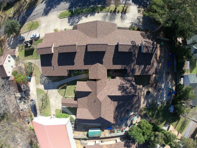 Overhead view of a brown-roofed building complex with multiple sections, surrounded by trees and a few other buildings.