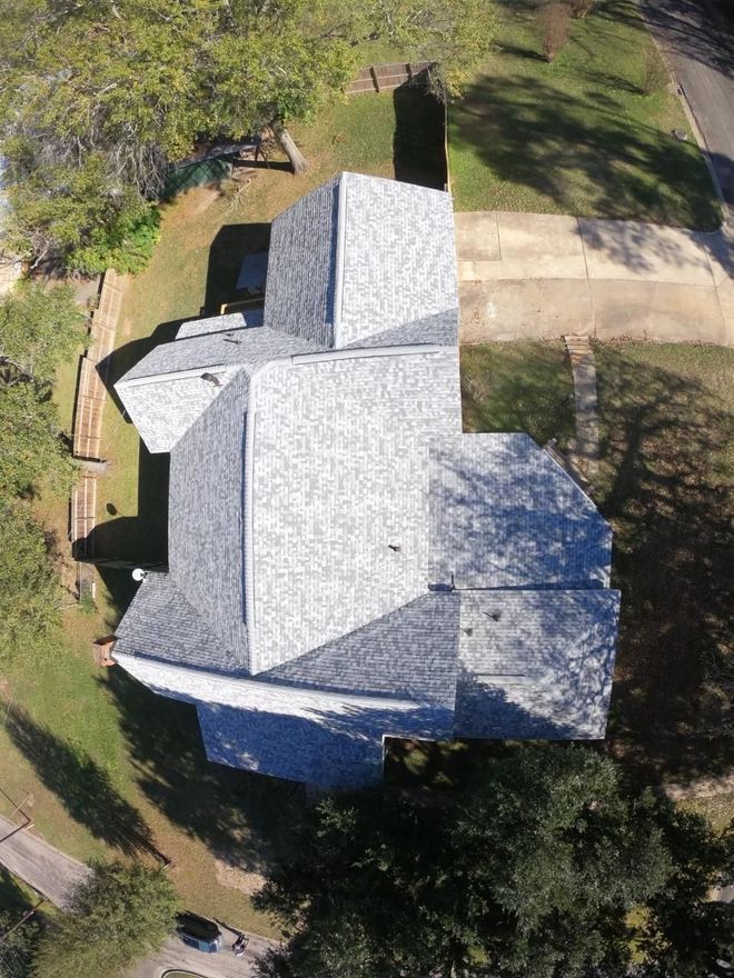 Overhead view of a house with a gray shingled roof, trees, and a driveway.