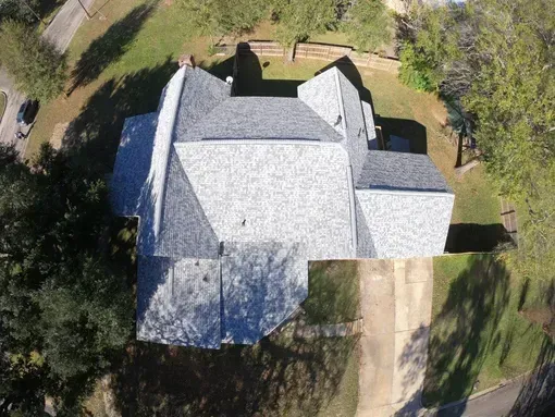 Aerial view of a gray-roofed house with a driveway surrounded by green grass and trees.