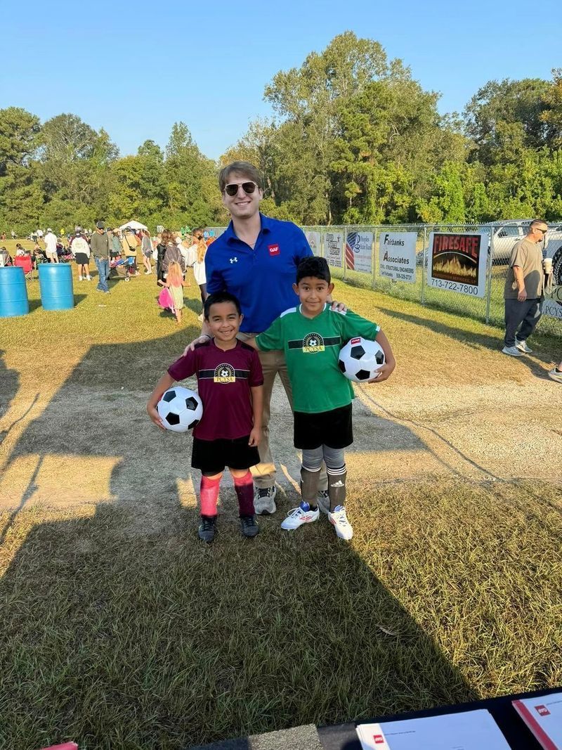 Coach and two soccer players with balls posing on grass field.