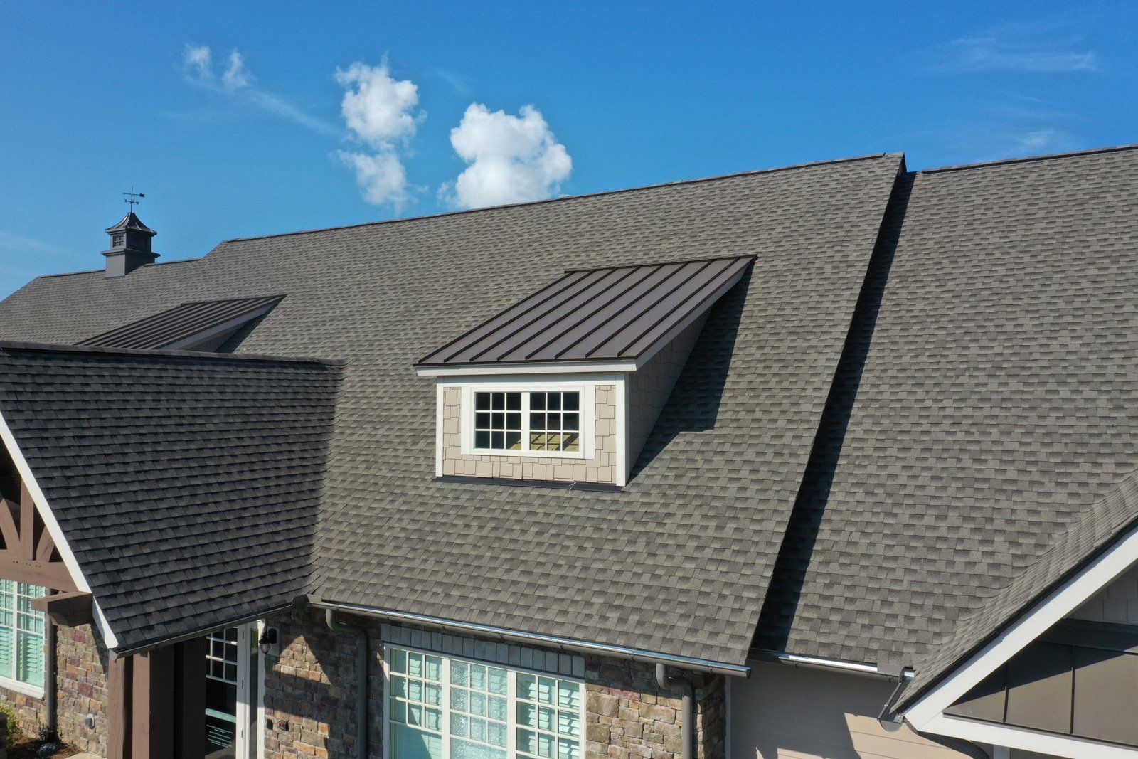 Dark gray shingled roof with a dormer, against a blue sky with clouds.