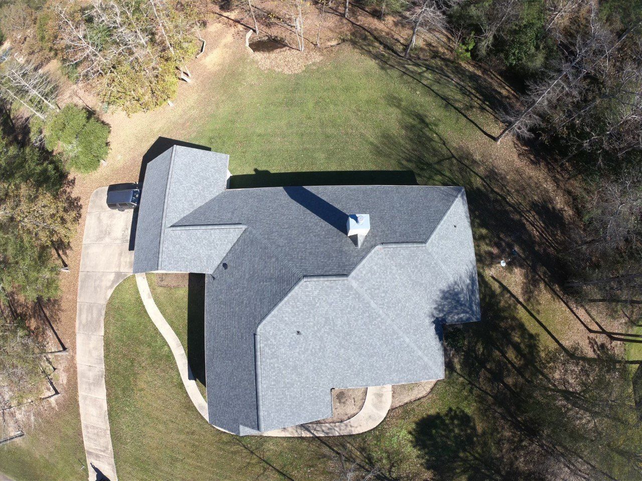 Overhead view of a house with a gray roof, surrounded by green grass and trees.
