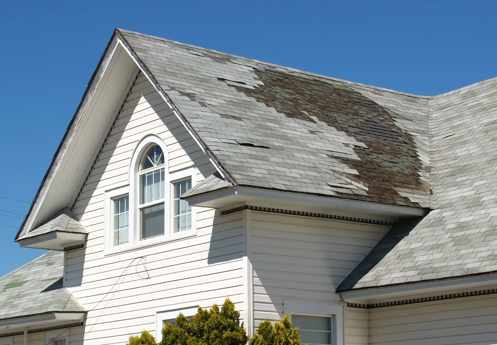White house with damaged roof and a clear blue sky.