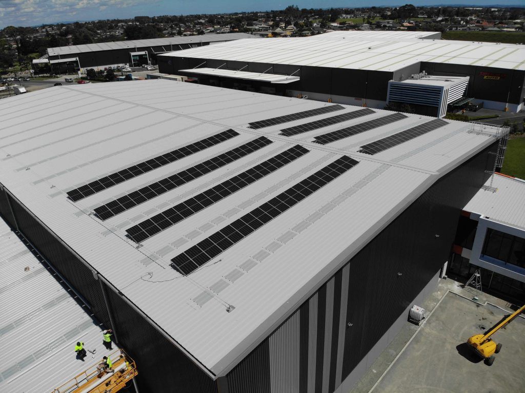 Aerial view of large warehouse rooftops with rows of solar panels and nearby industrial buildings