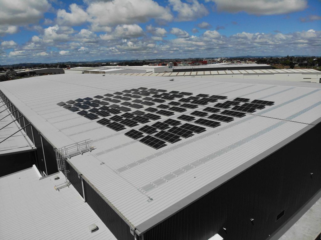 Rooftop solar panels on a large white industrial building under a cloudy sky